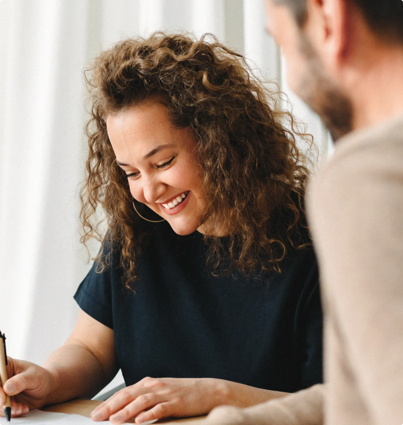 woman smiling signing a paper, joined by a man on her right
