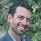 Evan Dreyer, Head of Risk and Finance at TOLA, standing in front of foliage backdrop