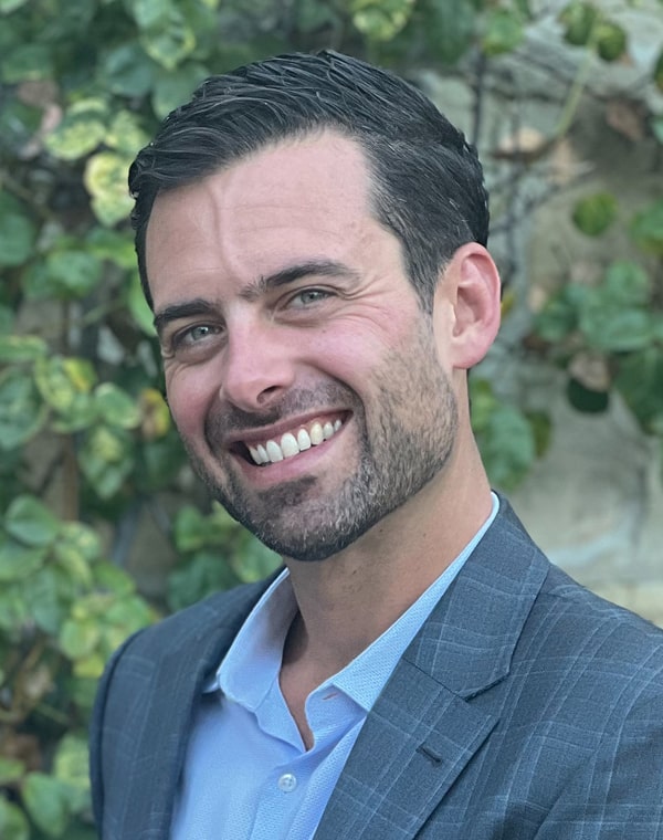 Evan Dreyer, Head of Risk and Finance at TOLA, standing in front of foliage backdrop